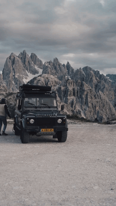 Rooftop tent from Roof Space being opened by a person on a Land Rover infront of a scenery of mountains.